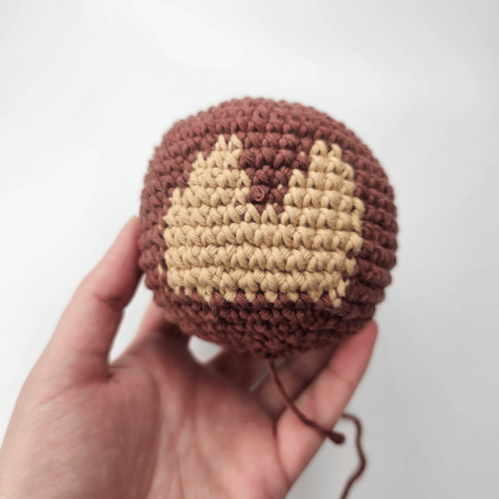 Free monkey lovey crochet pattern. This is the amigurumi monkey lovey head completed without embroidered or safety eyes at this point. The majority of the head is crocheted using dark brown yarn, with the face shape crocheted by changing colour to a light brown yarn.